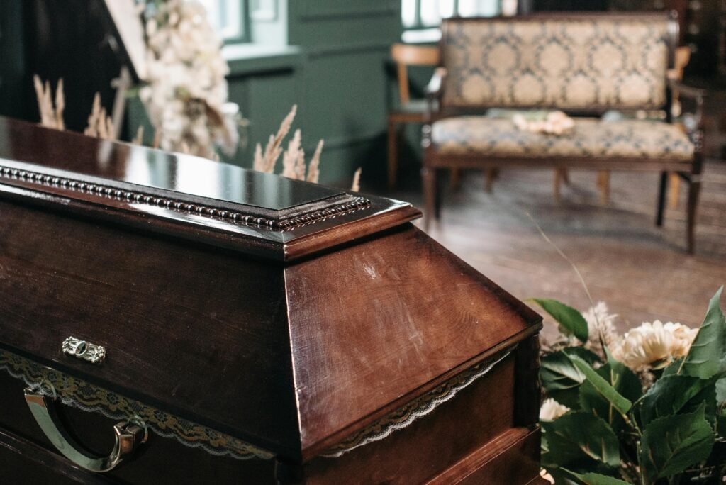 Derecho de Sucesión - Herencias Elegant wooden coffin surrounded by floral arrangements in an indoor funeral setting, capturing a somber mood.